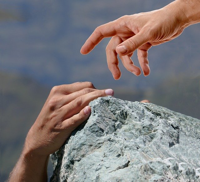две човешки ръце се протягат една към друга, един човек спасява друг на ръба на планинската бездна
