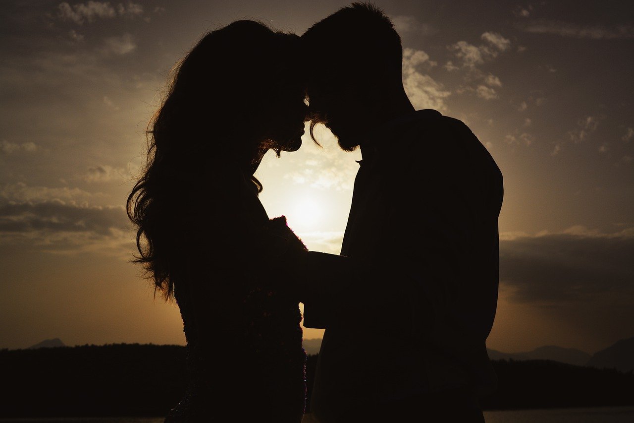 на фона на красив летен залез мъж и жена се целуват, като извивките на телата им оформят едно голямо сърце